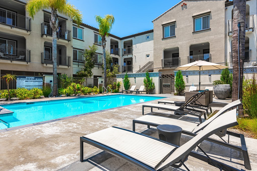 A pool area with sun loungers and a building in the background.