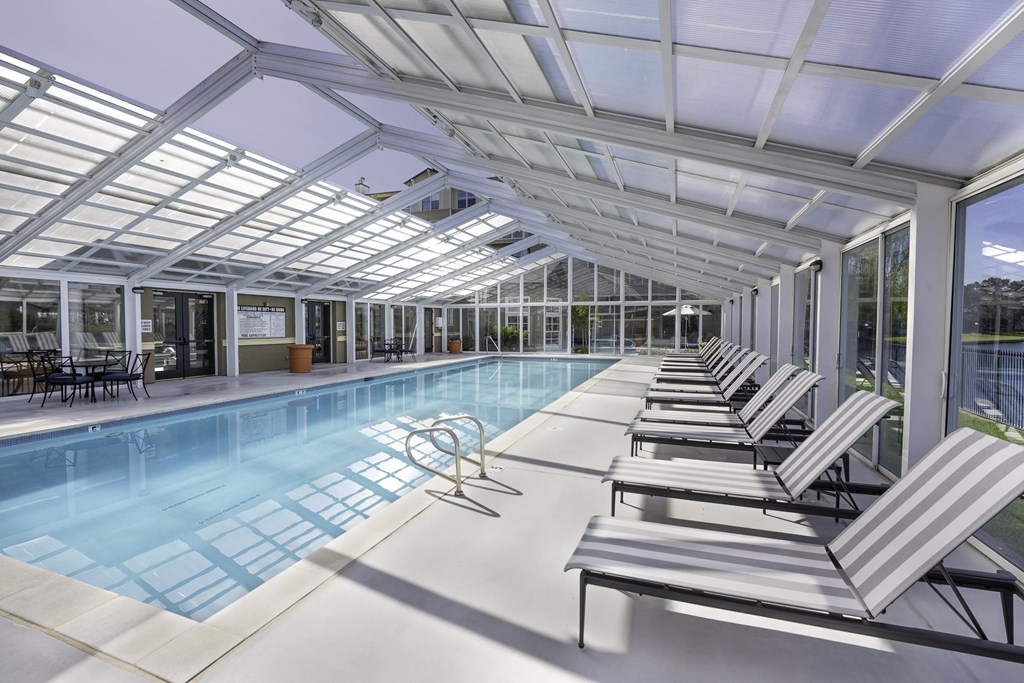the pool is under a glassed inrium with white lounge chairs
