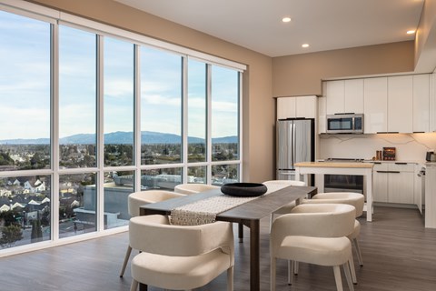 A modern kitchen with a dining table and chairs in front of large windows overlooking a cityscape.