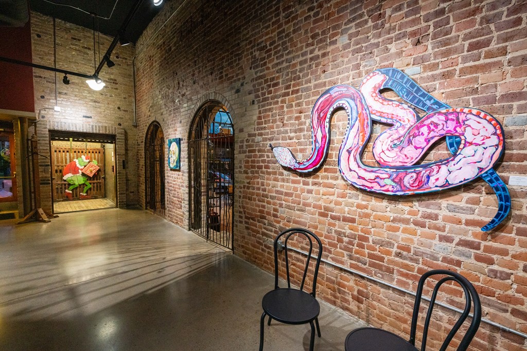 a large snake artwork on a brick wall in a room with chairs at Mihir Taylor, Texas 76574