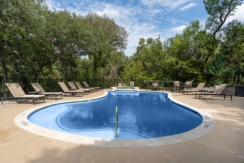 A round swimming pool surrounded by lounge chairs and trees.