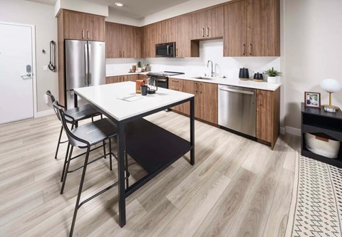 a kitchen with a table and a refrigerator Pet-Friendly Apartments in Walnut Creek - NoMA - Kitchen with Wood Cabinetry, Plank Luxury Flooring, Quartz Countertops and Stainless Steel Appliances at NoMa