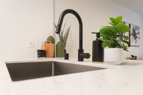 Kitchen sink with black faucet and white countertop at Noda Apartments, Washington