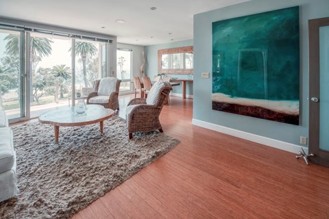 A living room with a large painting on the wall and a glass door leading to a balcony.