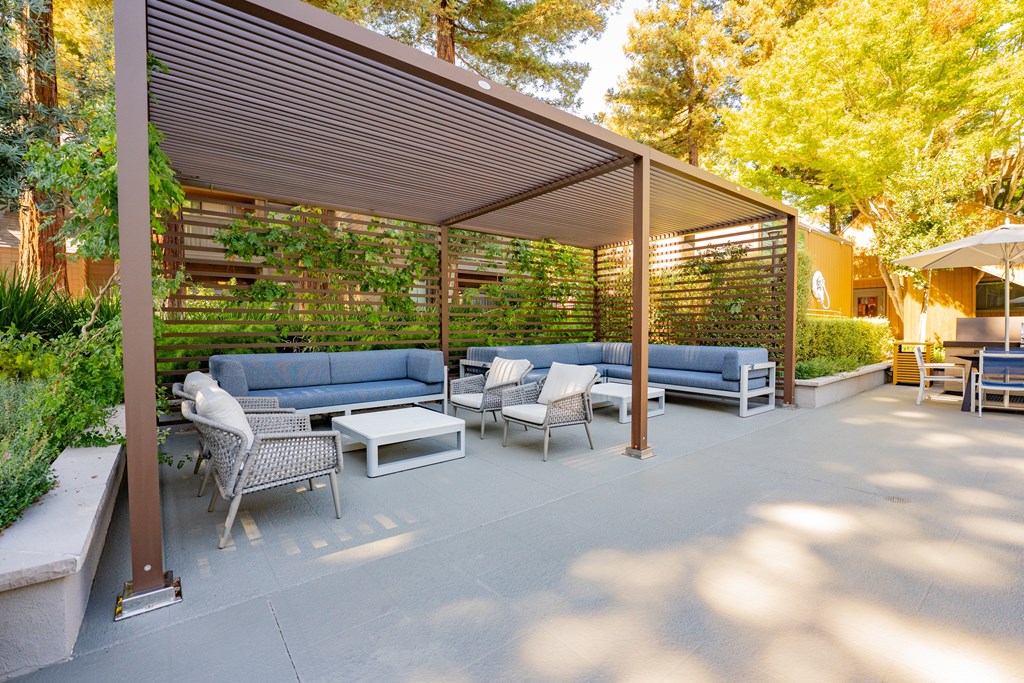 A patio with a couch, chairs, and a table under a pergola.