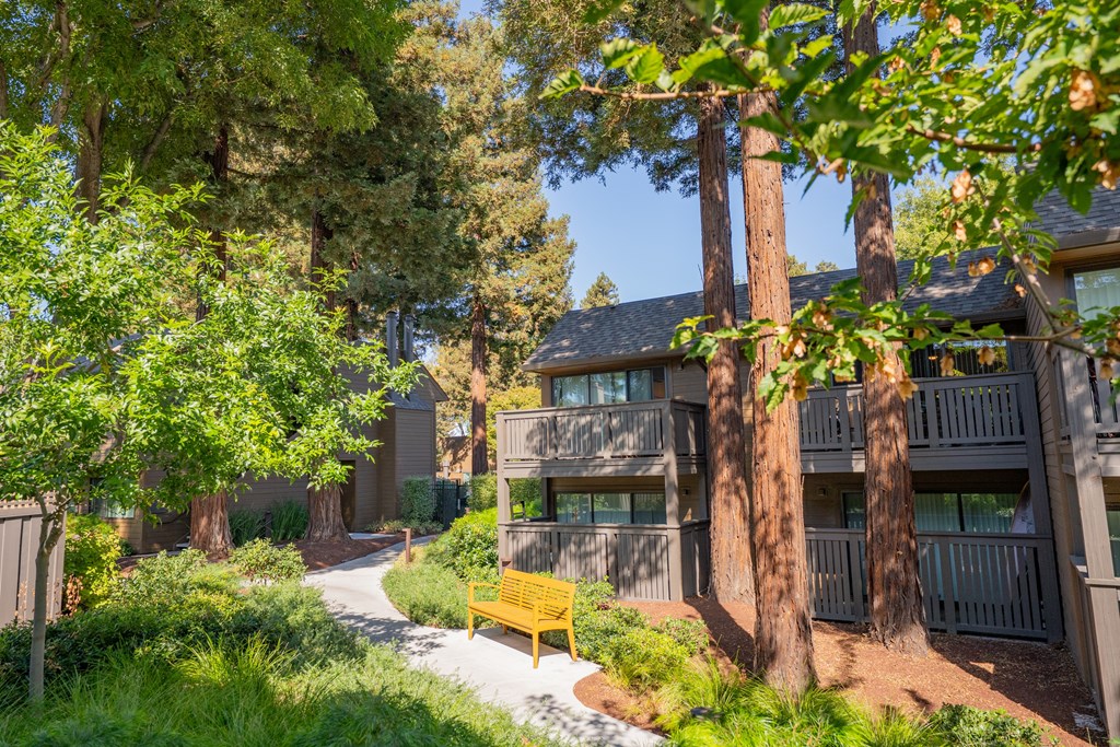 A yellow bench sits in front of a building with a tree in front of it.
