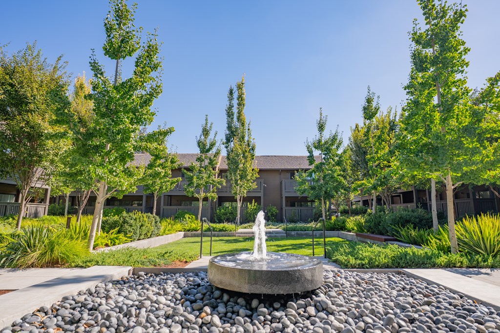 A fountain in the middle of a rock garden in front of a building.