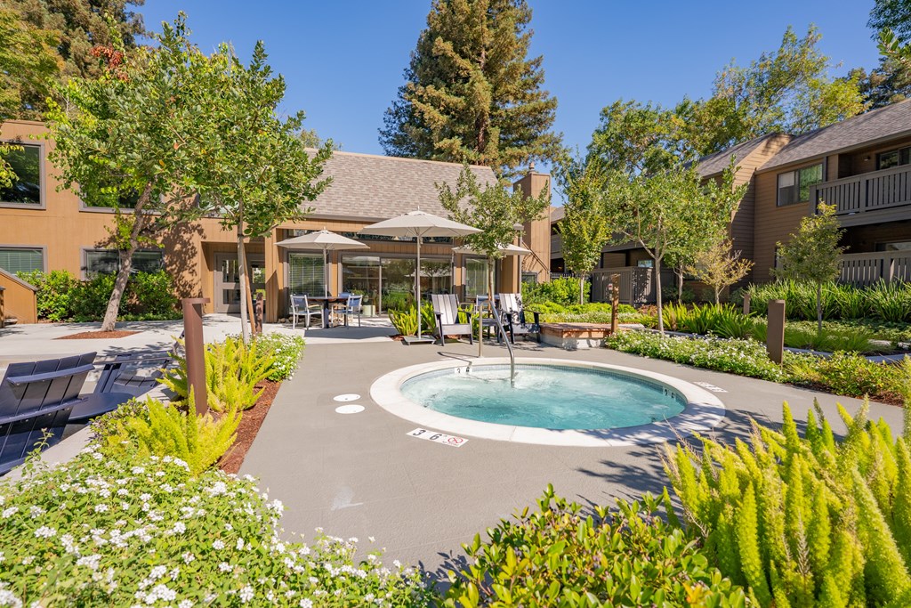 A pool surrounded by plants and trees with a building in the background.
