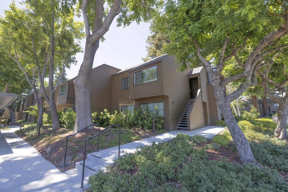 Apartment complex with a brown exterior is surrounded by green trees.