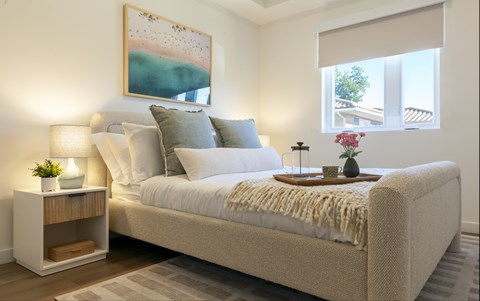 A bedroom with a large bed, a nightstand with a lamp, and a painting on the wall.