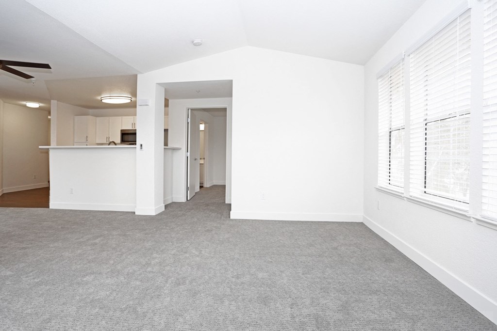 an empty living room with a kitchen in the background