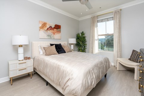 A bedroom with a large bed, a nightstand with a lamp, and a painting on the wall.