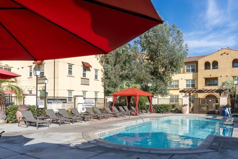 A pool area with a red umbrella and lounge chairs.