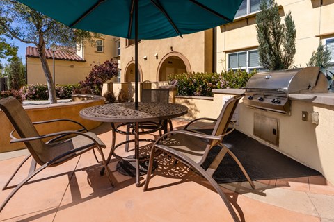 a patio with a grill and a table with chairs and an umbrella