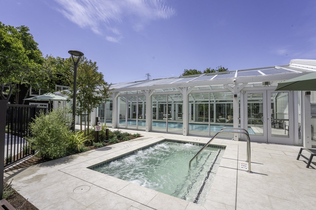 the pool and spa area of a house with a glass building