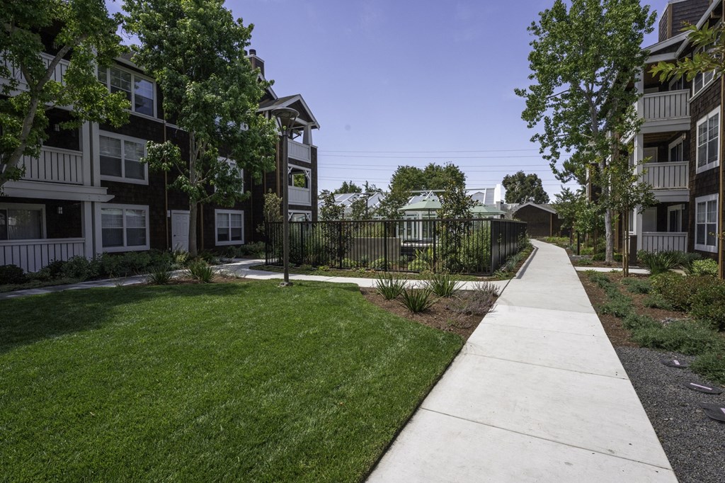 a sidewalk in front of an apartment building with grass and trees