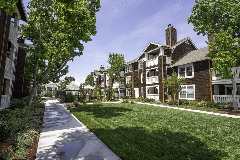 a sidewalk leading to an apartment complex with green grass and trees