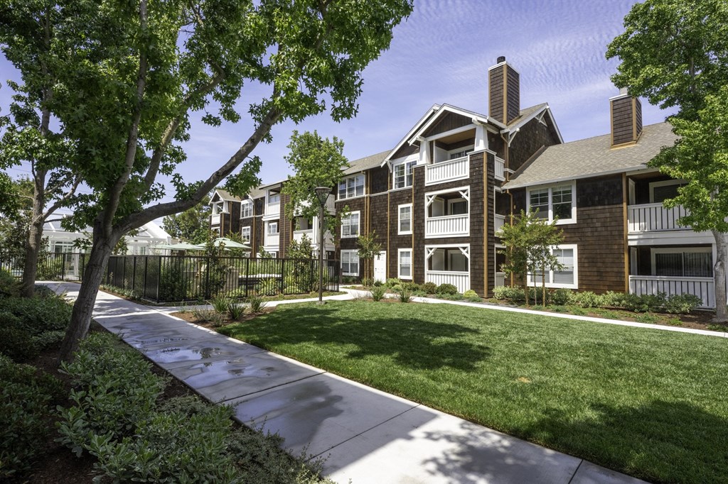 an exterior view of an apartment building with a lawn and sidewalk