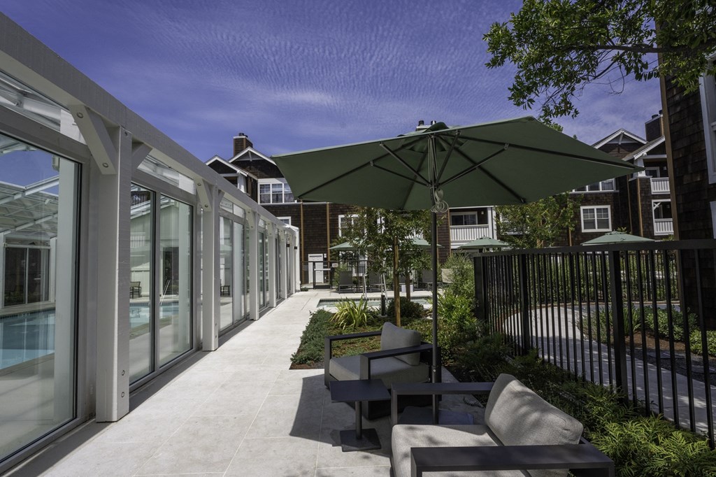 a patio with chairs and an umbrella next to a pool