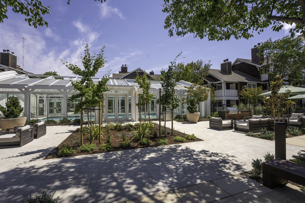 a courtyard with benches and trees in front of a white house