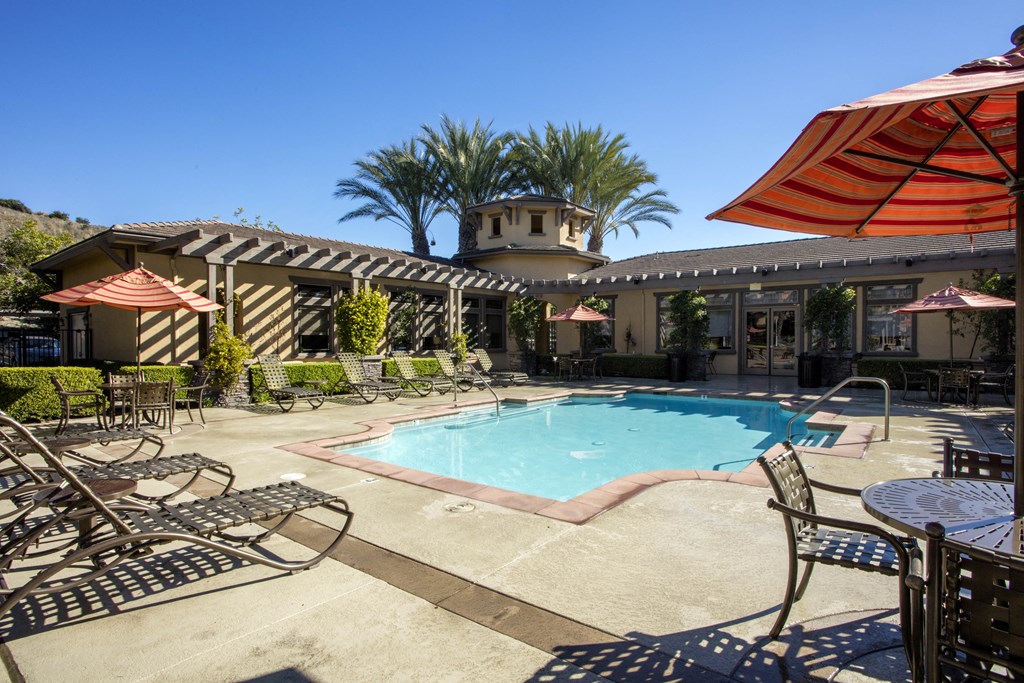 a swimming pool with lounge chairs and umbrellas in front of a hotel at 55+ Remington at Ladera Ranch, Ladera Ranch