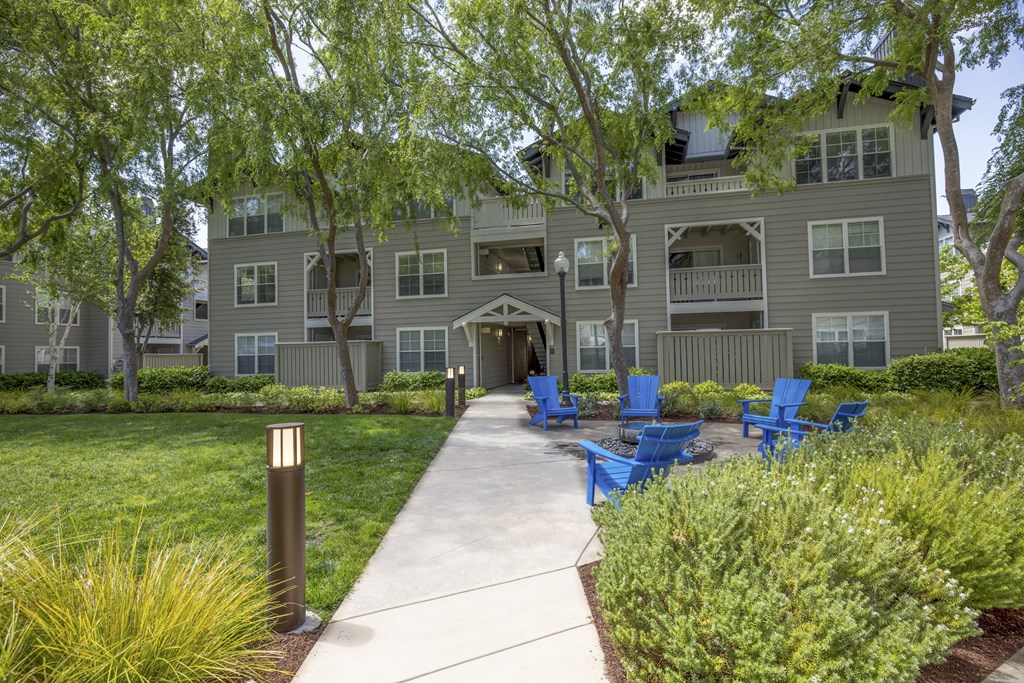 a walkway with blue chairs in front of an apartment building