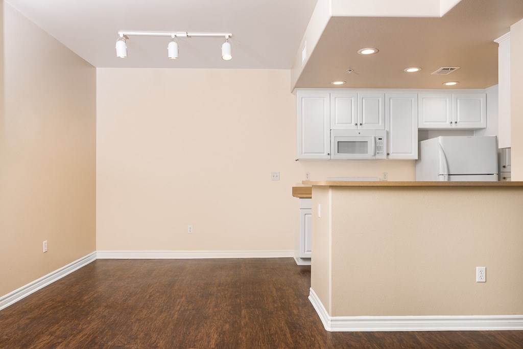 an empty living room with a kitchen in the background