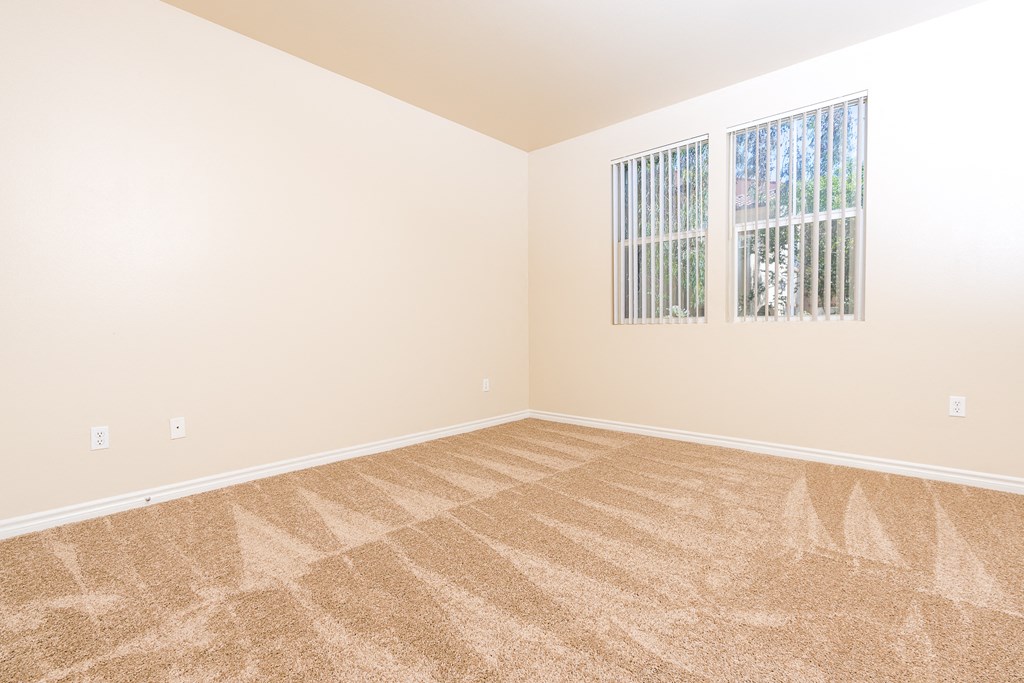 a bedroom with beige carpet and two windows