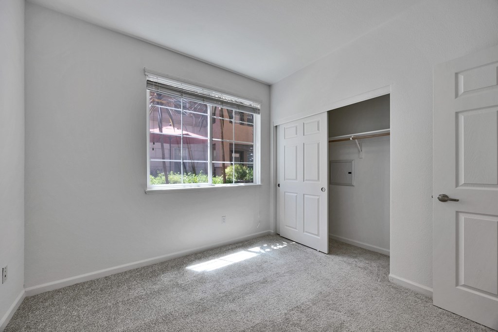 North San Jose, CA Apartments - Aviara - Unfurnished Bedroom with Carpeted Flooring, White Walls, Spacious Closet with Sliding Door, and Large Window.