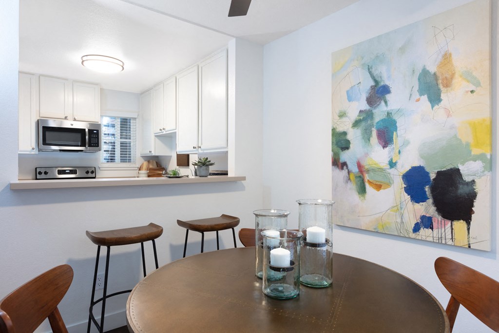 A modern kitchen with a wooden table and chairs, a microwave, and a painting on the wall.