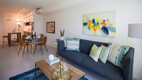 A living room with a blue couch and a painting on the wall.
