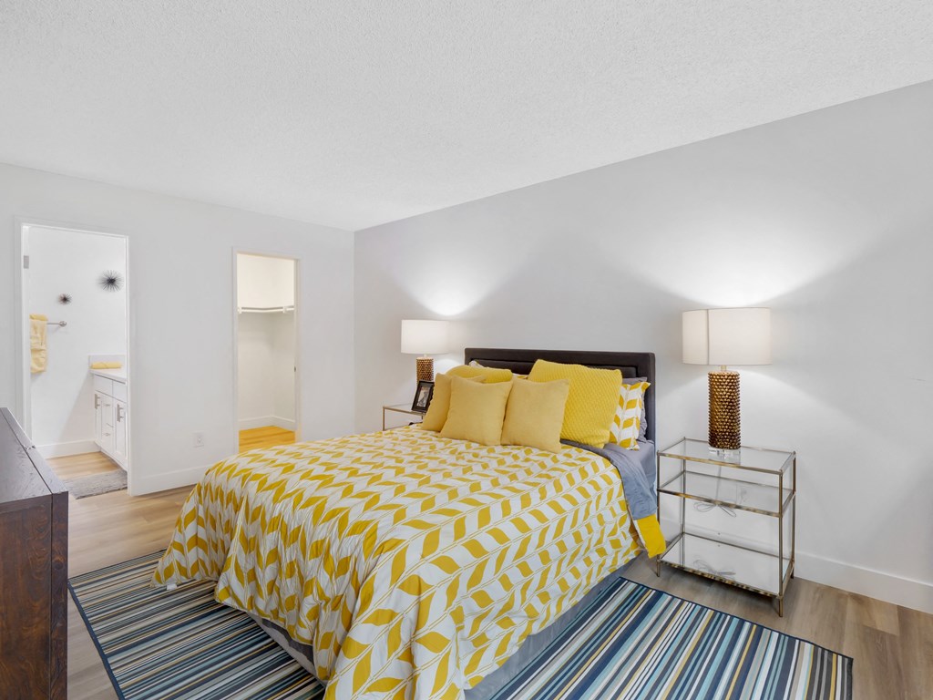 A bedroom with a bed covered in yellow and white bedding at Verandas Apartments, West Covina, California