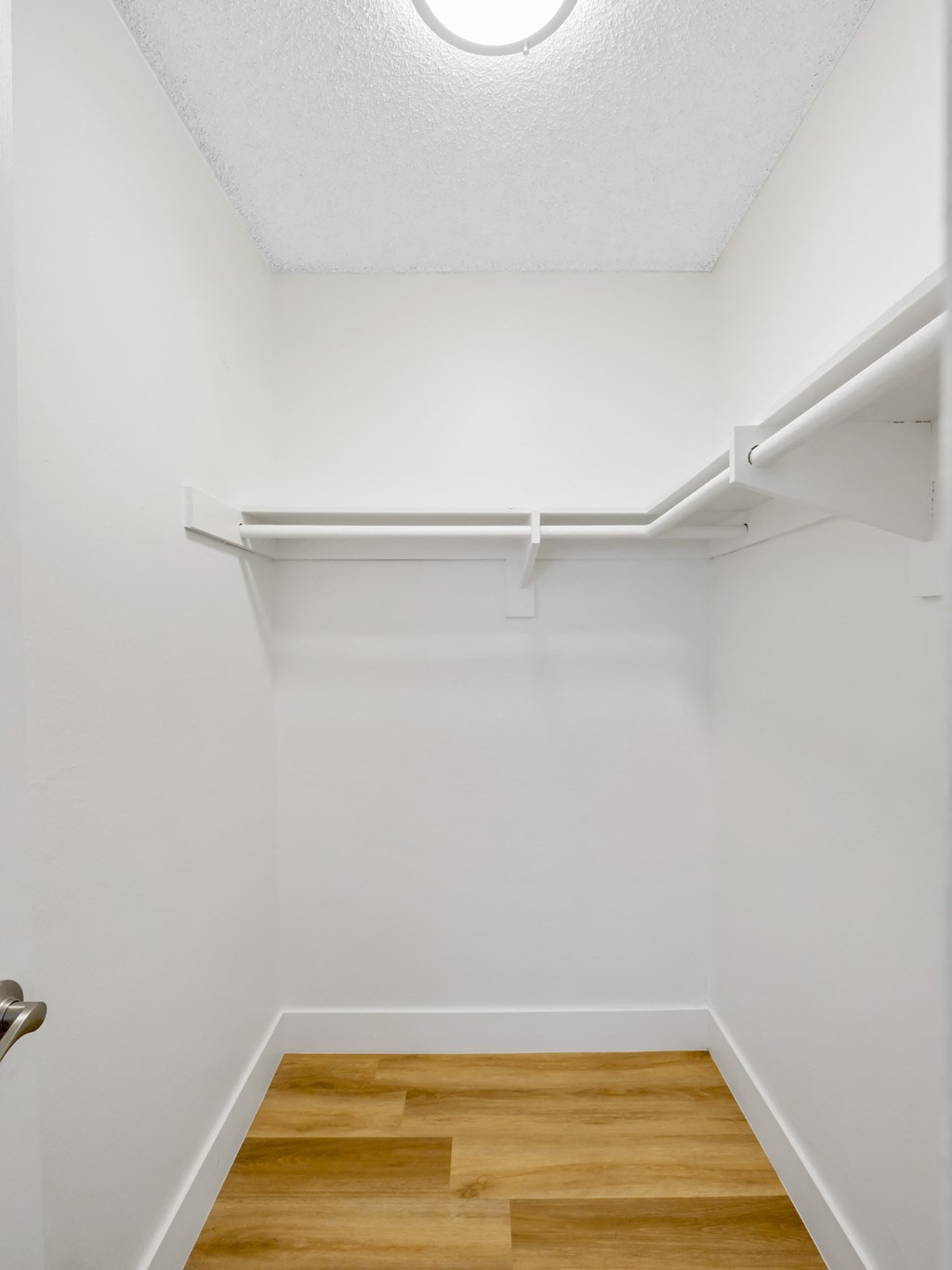 A white hallway with a wooden floor and a door on the left at Verandas Apartments, California