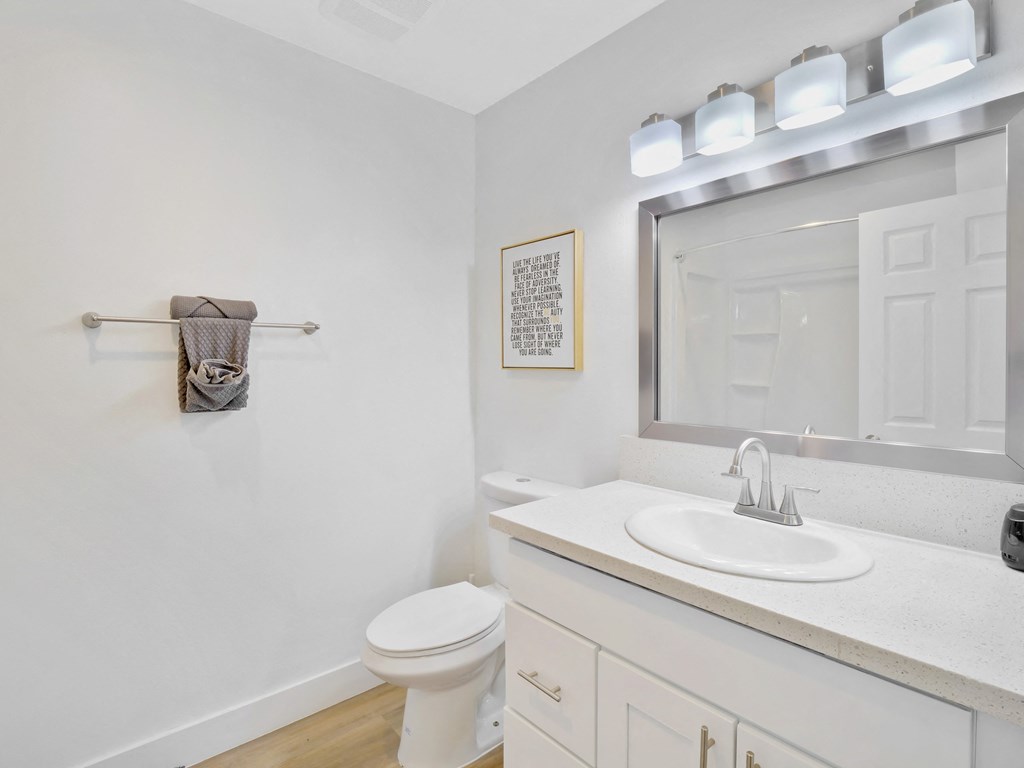 A white bathroom with a toilet, sink, mirror, and a towel rack at Verandas Apartments, West Covina, 91791