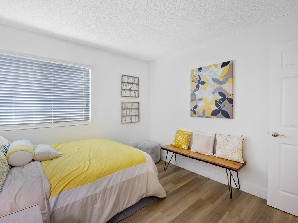 A bedroom with a bed, bench, and artwork at Verandas Apartments, West Covina, California