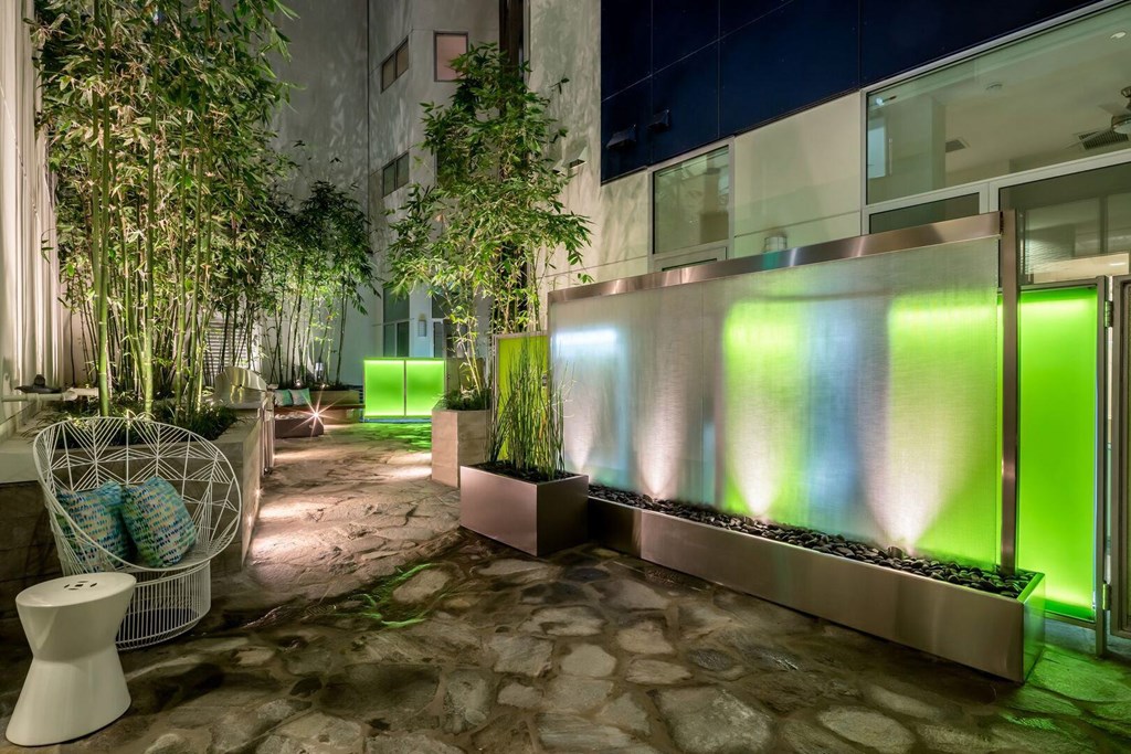 A modern outdoor space with a stone floor, a white chair, and a green lighted wall.