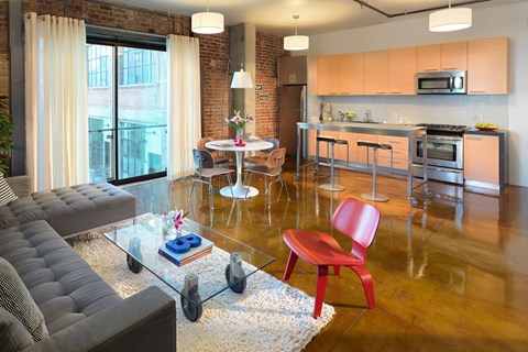 A modern living room with a grey sofa, a red chair, and a glass table.