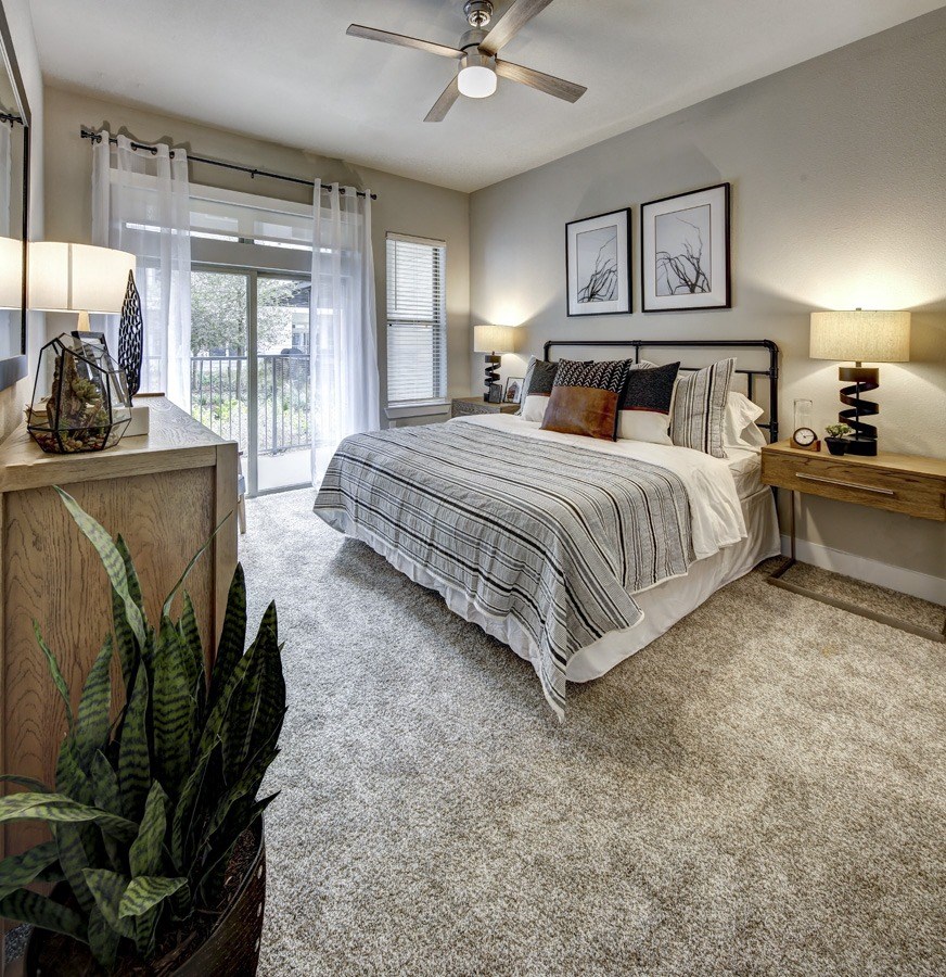 1 And 2-BR Apartments In Austin, TX - Arise Riverside - Spacious Bedroom With Ceiling Fan, Plush Carpet Flooring, A Window, And Access To Balcony.