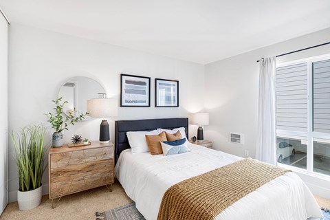 A bedroom with a bed, nightstand, and a plant.