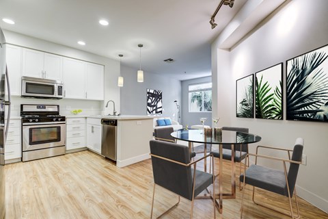 Two-Bedroom Apartments in Milpitas, CA - Ilara Apartments - Kitchen With White Cabinets, Stainless Steel Appliances, Pendant Lighting, Glass Dining Table, Botanical Wall Art, And Wood Style Flooring.