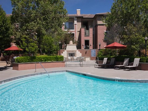 Apartments in North Natomas, Sacramento, CA, with In-Unit Washer and Dryer - Granite Point Apartments - Swimming Pool With Clear Blue Water, Poolside Lounge Chairs, and Red Umbrellas.