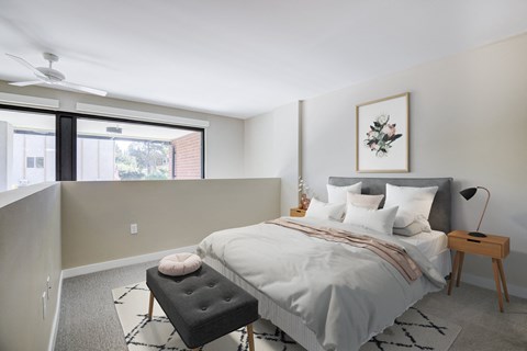 Seattle, WA, Apartments With In-Unit Washer and Dryer - Origin - Loft-Style Bedroom with Carpeting, a Bed, Two Bedside Tables, a Lamp, a Ceiling Fan, and a Barrier Overlooking the Rest of the Unit Interior.