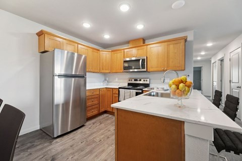 Dog-Friendly Apartments in Vancouver, WA - Prairie Home Apartments - Kitchen with Island, Plank Flooring, Shaker Cabinetry, Recessed Lighting, Stainless Steel Appliances, and Chairs.