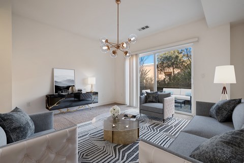 Pet-Friendly Apartments in Novato, CA - Millworks - Living Room With Gray Sofas, Tufted Accent Chairs, Round Coffee Table, Modern Chandelier, Patterned Rug, And Sliding Glass Door To Patio.