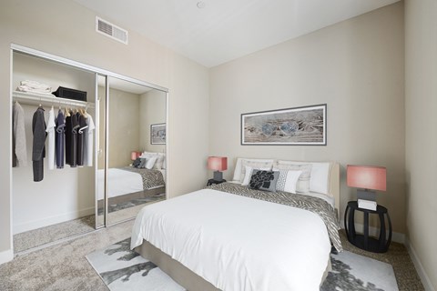 One Bedroom Modern Apartments in Long Beach CA - Urban Village - Carpeted Bedroom with a Large Bed, a Large Mirror-Door Closet, Black Nightstands, and Beige Walls
