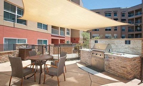 2-Bedroom Modern Apartments In San Rafael, CA - Rafael Town Center - BBQ Area With Viking BBQ Grill, Tables, And Chairs Under Shade.