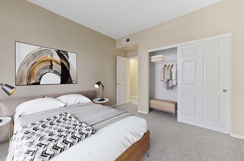 Dog-Friendly Apartments in Upland, CA - Park Central Apartments - Bedroom with Carpet Flooring, Large Bed, Nightstands, Lamps, Abstract Wall Art, and Oversized Closets with a Sliding Door.