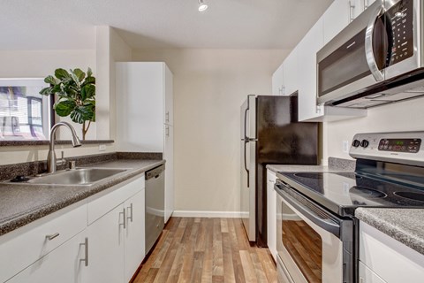 Pet-Friendly Apartments in San Rafael, CA - Rafael Town Center - Bright Galley Kitchen with White Cabinets, Double Sink, Speckled Countertops, Stainless Appliances, and Wood-Style Flooring.