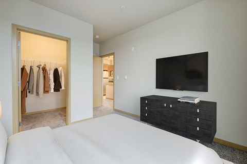 A bedroom with a large bed and a wardrobe with clothes hanging.