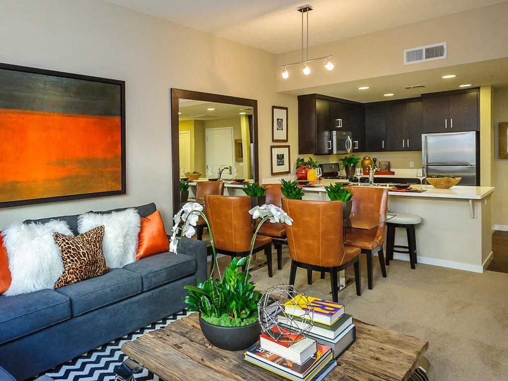 Apartments in Foster City, CA - The Plaza - Living Room with Carpeting, Couch, Coffee Table, Beige Walls, Framed Wall Art, Large Mirror, and View of Dining Area and Kitchen